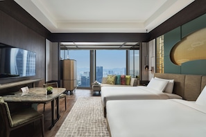 Quarto de hotel com uma televisão grande, uma mesa de jantar, duas camas, vista para a cidade e design moderno.