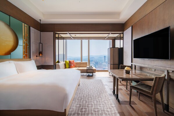 A modern hotel room with a large bed, a dining area with a table and chairs, a flat-screen TV, and a city view through large windows. - Park Hyatt Shenzhen (Shenzhen)