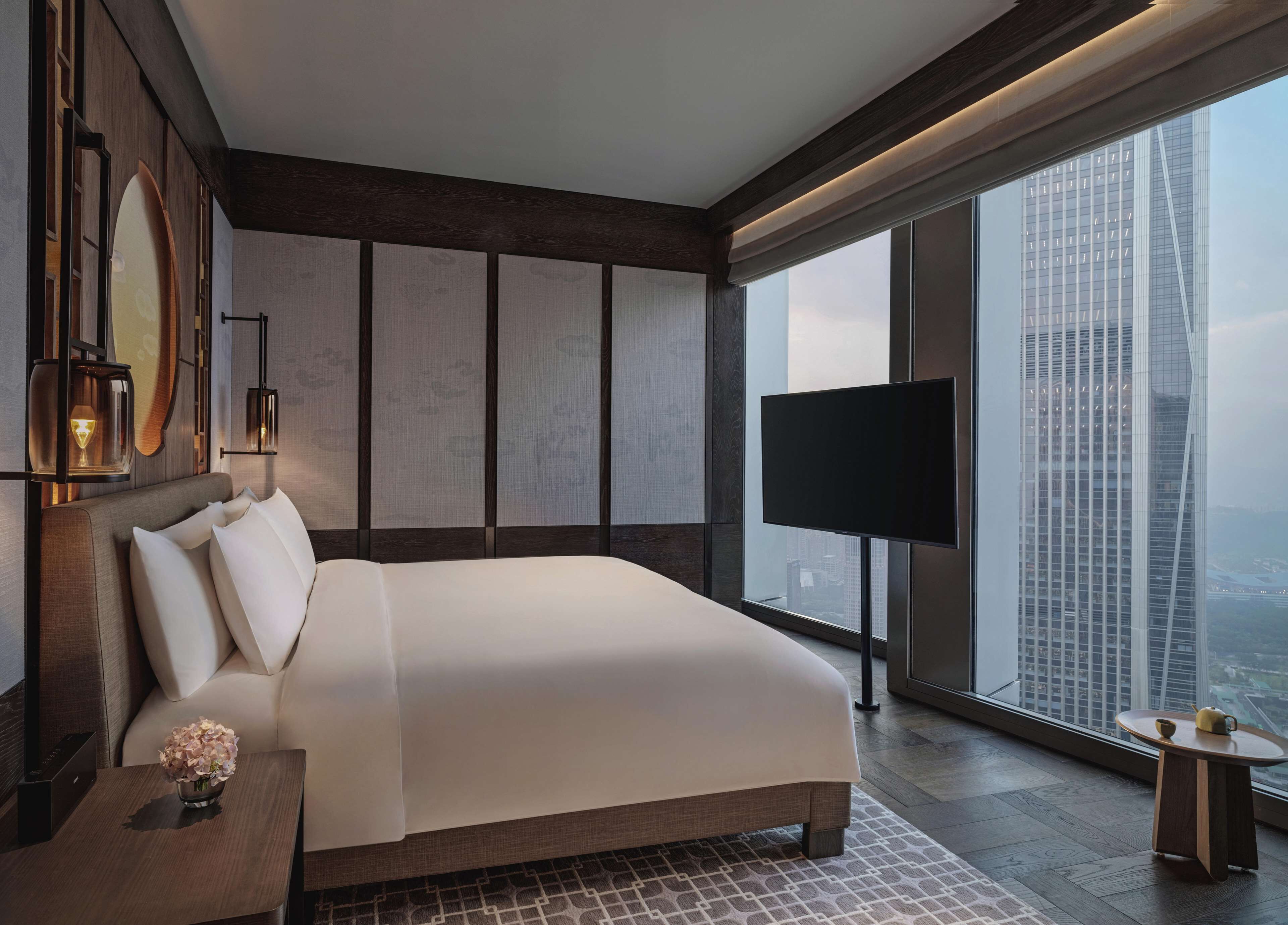 A modern hotel room with a large bed, a TV, and a city view.