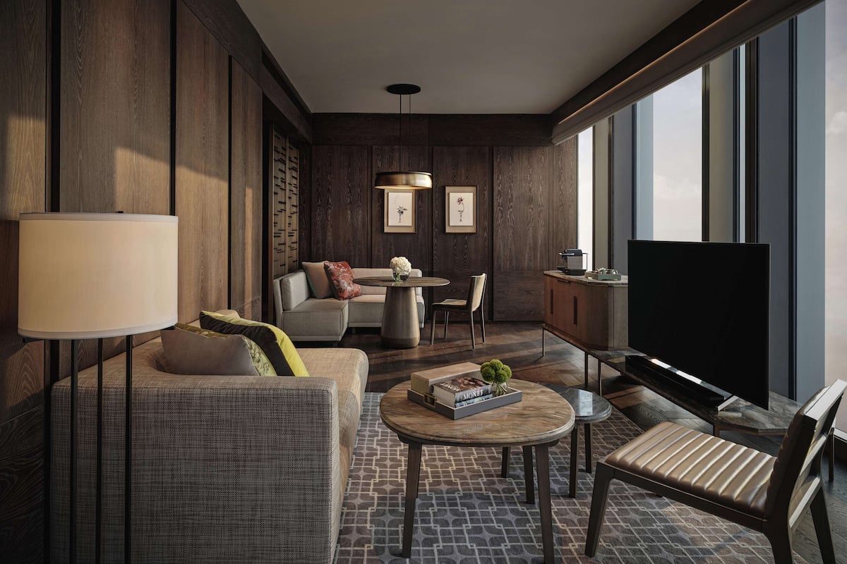 Una habitación de hotel moderna con sofá, sillón, una mesa de centro redonda y televisor.