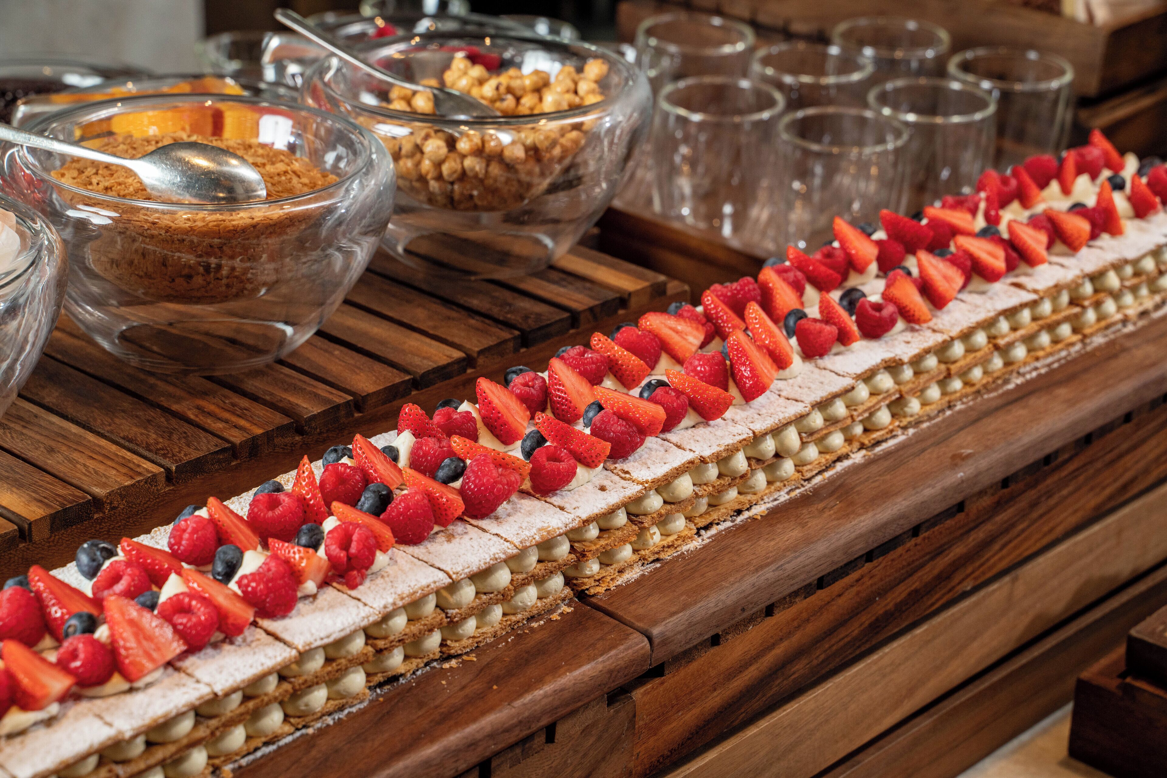 A long dessert tray with strawberries, blueberries, and raspberries on a wooden table.