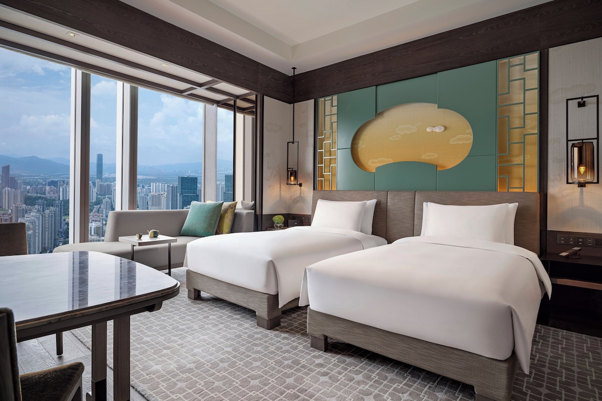 A hotel room with two beds, a dining table, a city view, and modern decor.