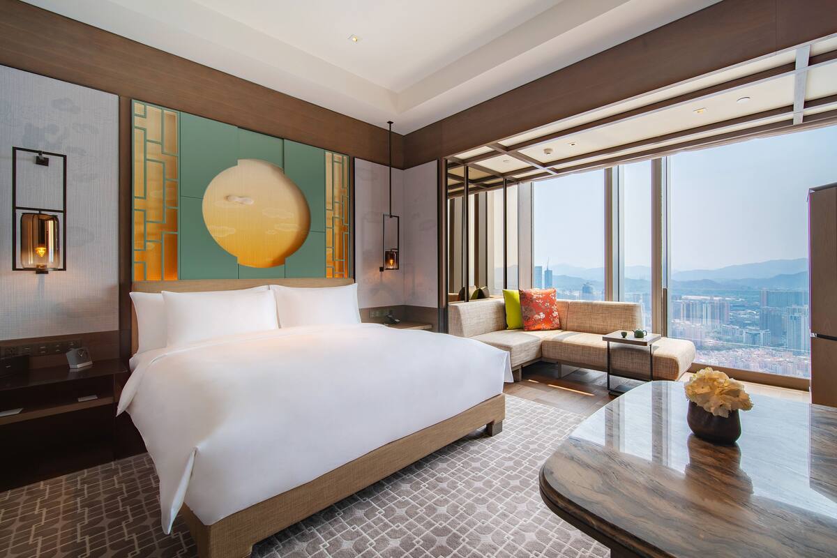 Ein modernes Hotelzimmer mit einem großen Bett, einer Sitzecke mit Ausblick und einem großen Fenster auf die Stadt.