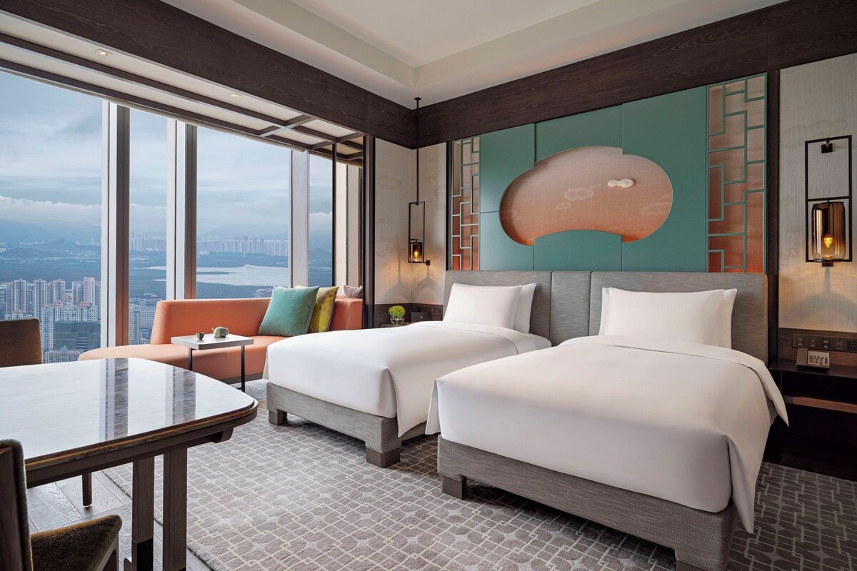 Habitación de hotel con dos camas, un sofá, una mesa de comedor y vistas a la ciudad.
