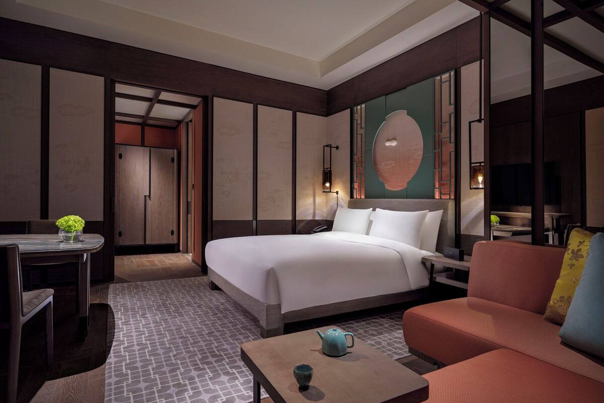 Ein Hotelzimmer mit Bett, einer Couch, einem Tisch mit Teekanne, einem Schreibtisch und einer Wand mit einem dekorativen Wandpaneel.