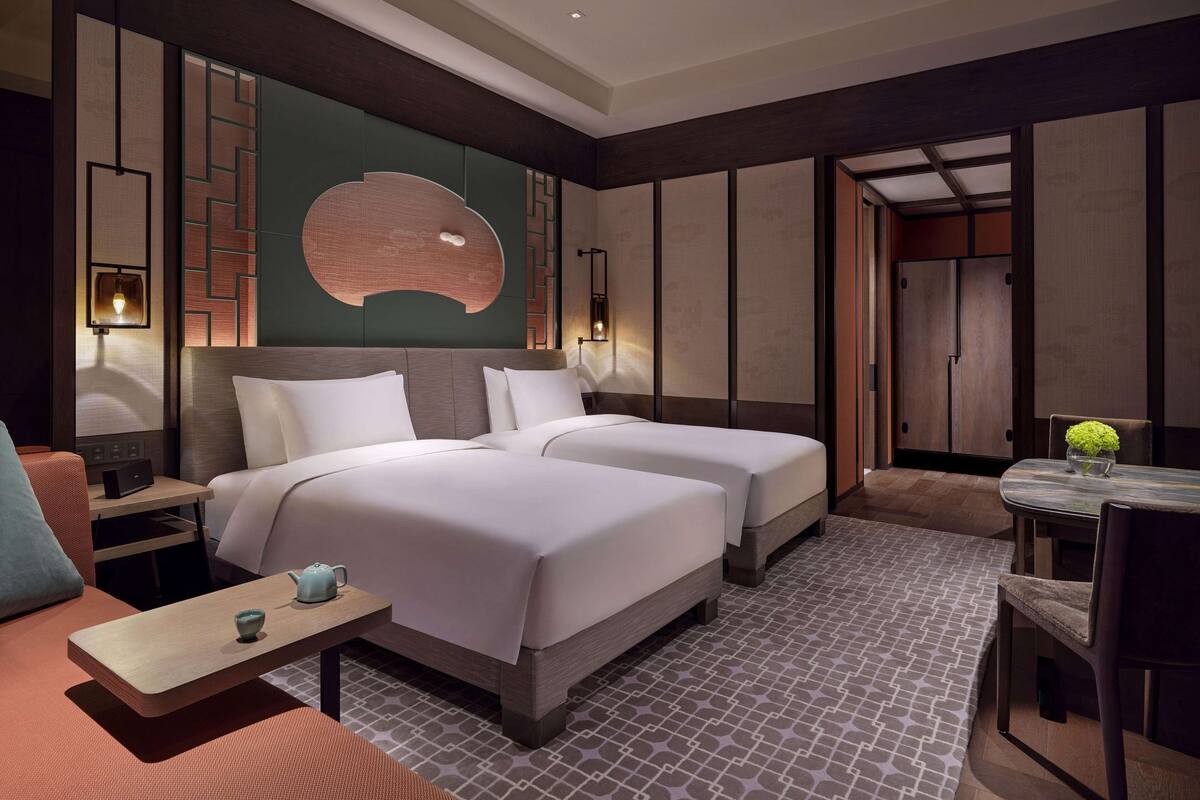 Habitación de hotel con dos camas, una mesita con un hervidor de agua, una silla y una mesa de comedor con un florero.