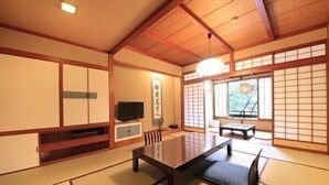 Ein traditioneller japanischer Raum mit Tatami-Böden, einem niedrigen Tisch, einem Fernseher und Schiebetüren.
