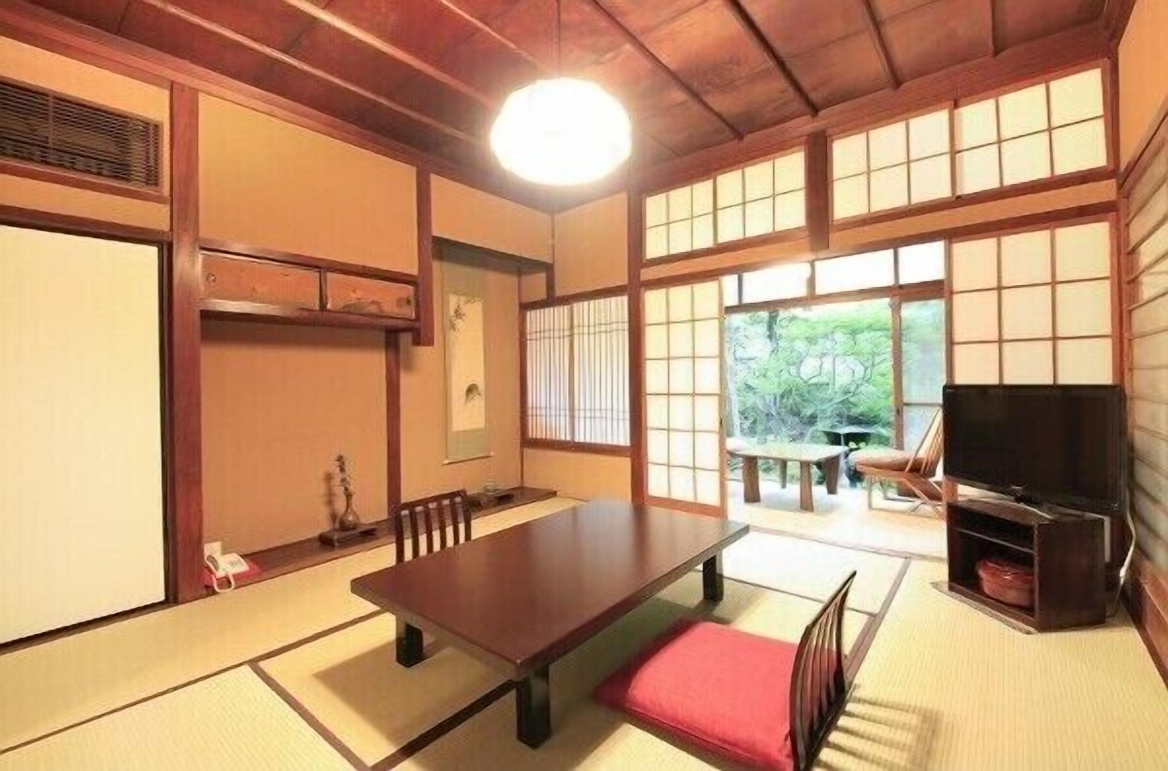 Ein traditioneller japanischer Raum mit Tatami-Böden, einem niedrigen Tisch, einem Fernseher und Schiebetüren.