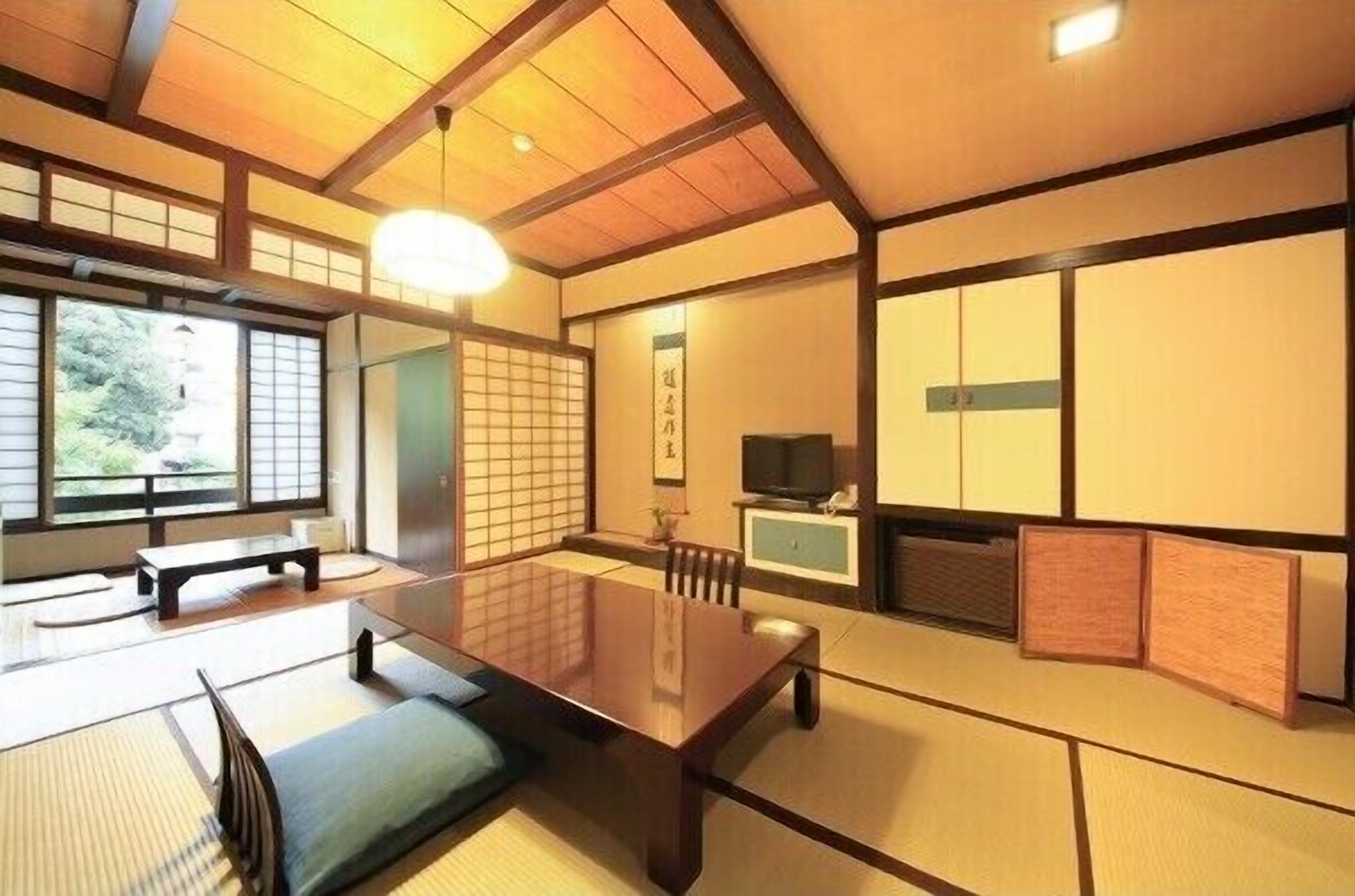 Ein traditioneller japanischer Raum mit Tatami-Bodenbelag, einem niedrigen Tisch, Schiebetüren und einem Fernseher.