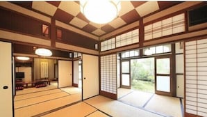 Ein traditioneller japanischer Raum mit Tatami-Böden, Schiebetüren und Blick auf Grünflächen.