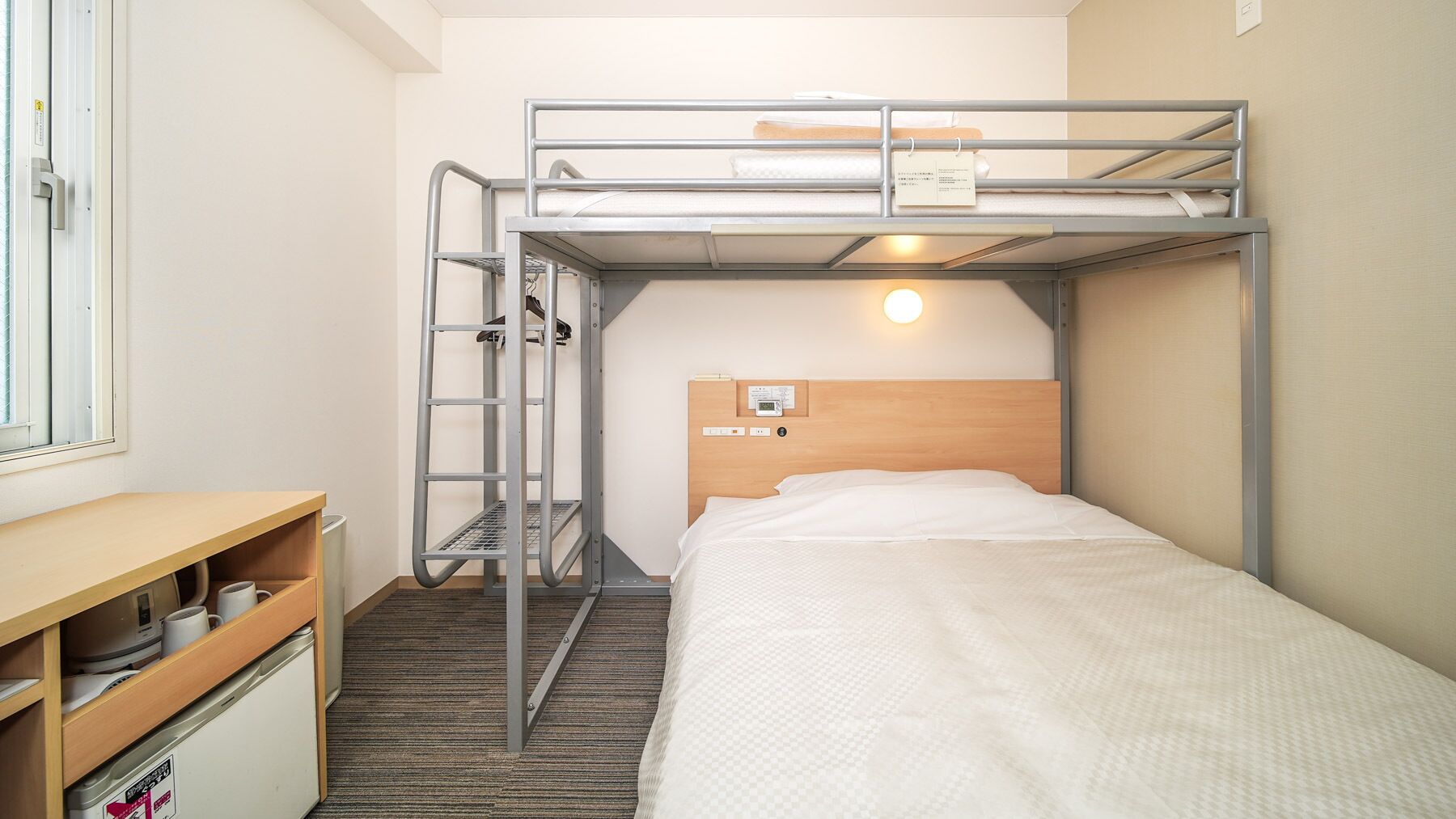 Una cama individual con cabecera de madera, un escritorio con una silla y una ventana pequeña.