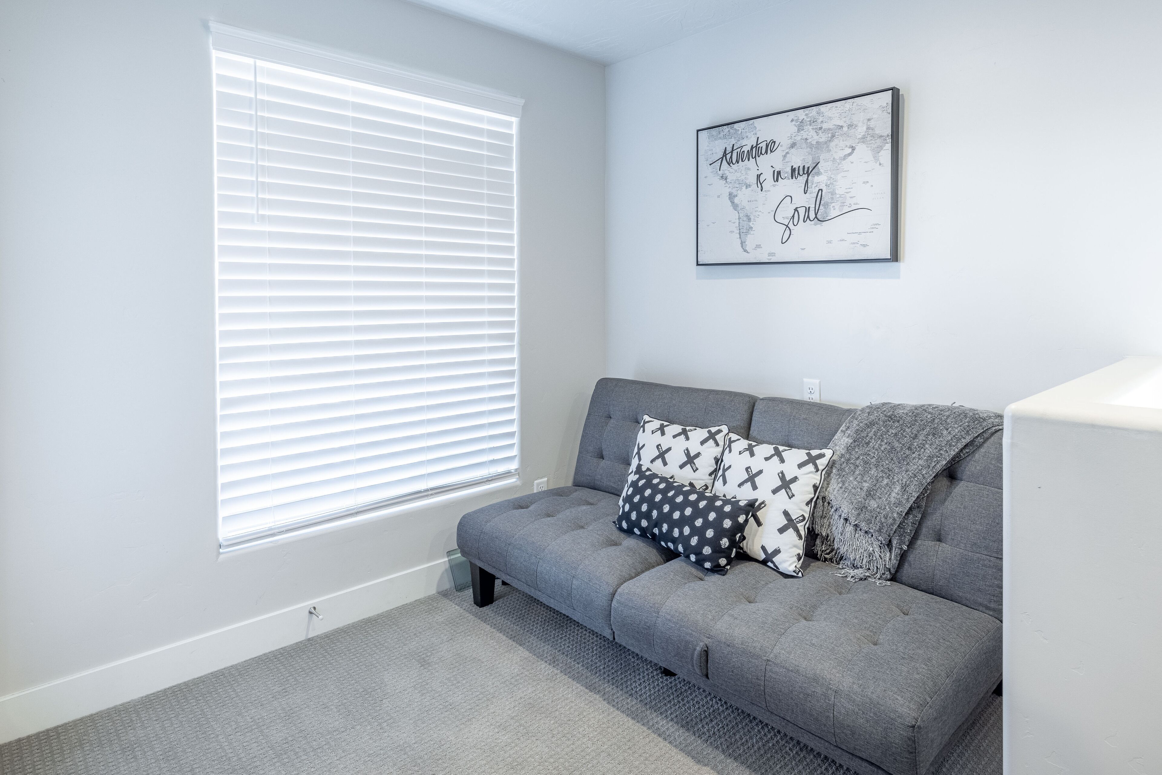 A modern living room with a grey sofa, patterned pillows, a grey throw blanket, and a framed inspirational quote on the wall.