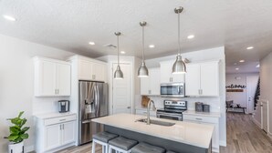 A modern kitchen with white cabinetry, stainless steel appliances, and a central island with bar stools. - Modern 3-King 4BR Sleeps 13 - Rooftop Deck (St. George)