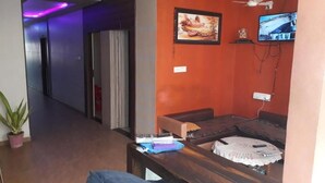 A living area with a sofa, a coffee table, and a television mounted on the wall. - Hotel Atithi (Mahesana)