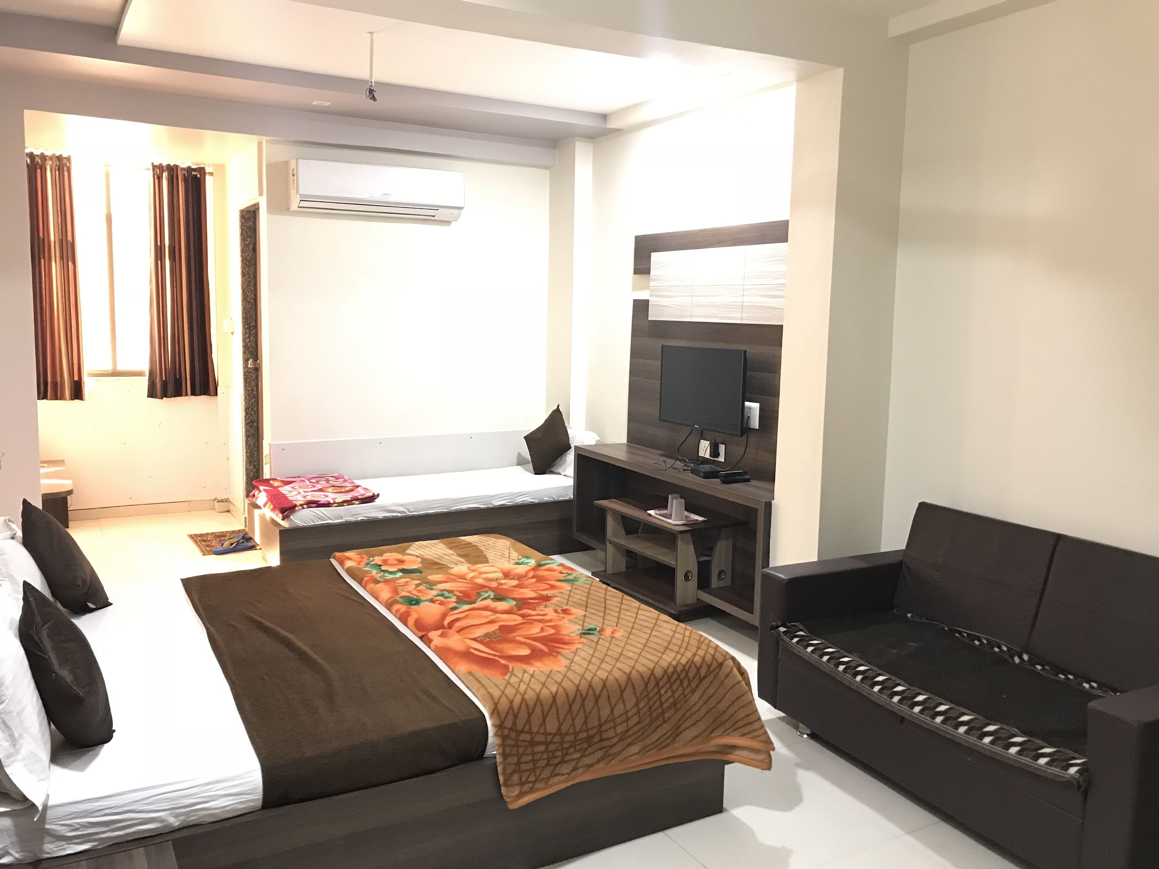 A modern hotel room with a bed, a sofa, a TV, and an air conditioning unit.