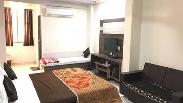A modern hotel room with a bed, a sofa, a TV, and an air conditioning unit.