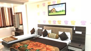 A modern hotel room with a large bed, a bedside table, a nightstand, and a wall-mounted TV. - Hotel Atithi (Mahesana)