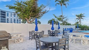Patio esterno con tavoli e sedie, barbecue e area piscina.