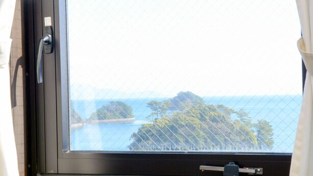 Una finestra con vista su un paesaggio costiero, con alberi e un tratto d'acqua.