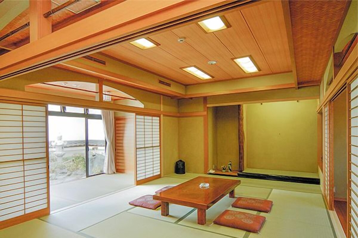 Une pièce de style japonais traditionnel, avec un sol recouvert de tatamis, une petite table en bois, des portes coulissantes et une vue par la fenêtre.