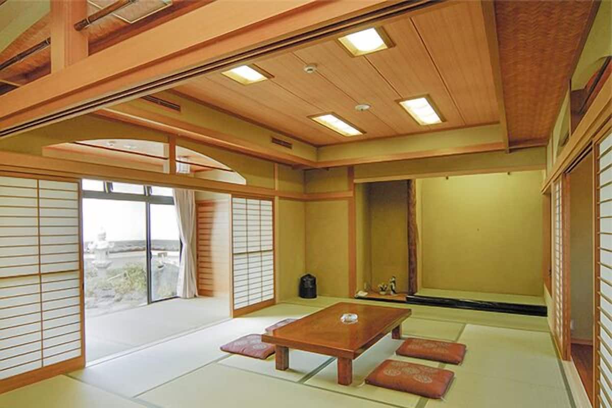 A traditional Japanese room with tatami flooring, a low wooden table, sliding doors, and a view through the window.