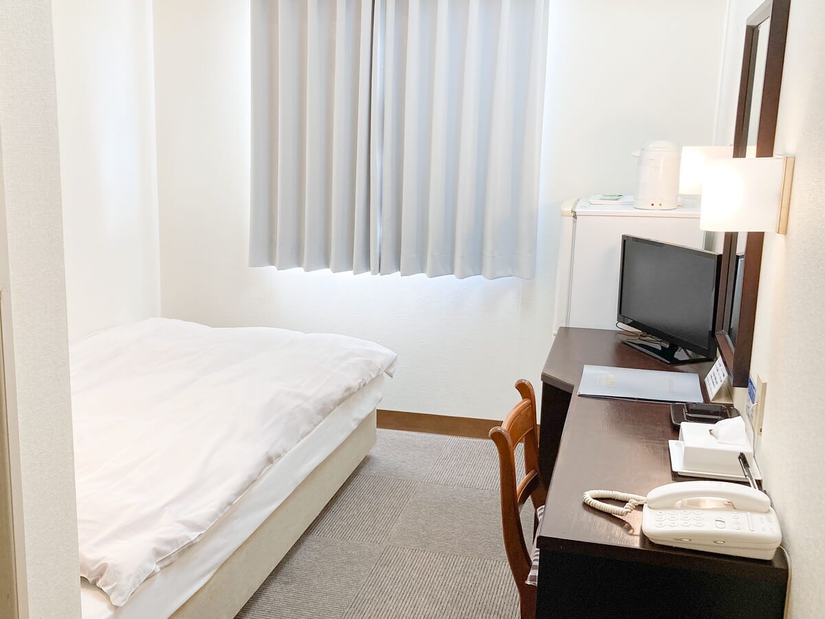 Una habitación de hotel con una cama, un escritorio con computadora, un teléfono y un televisor.