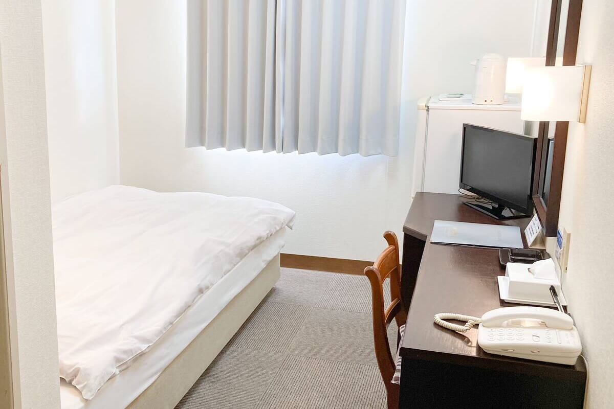 A hotel room with a bed, a desk with a computer, a telephone, and a television.
