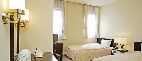 A hotel room with two beds, a desk, a chair, a lamp, a nightstand, and a window with curtains.