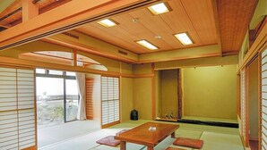 Una tradizionale stanza giapponese con pavimento in tatami, un tavolino in legno, porte scorrevoli e vista dalla finestra.