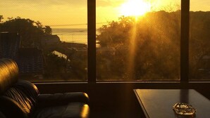 Una stanza con vista sul tramonto attraverso ampie finestre, un divano e un tavolo.