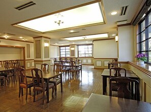 Un vaste espace dédié à la salle à manger, avec de nombreuses tables et chaises, de grandes fenêtres et un lustre.