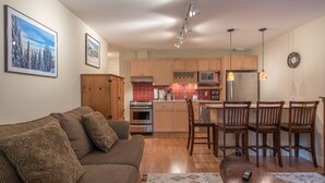 Ein gemütliches Wohnzimmer mit einer Couch, einem Essbereich mit Stühlen, einer Küche mit Holzschränken, einem Herd und einem Kühlschrank.