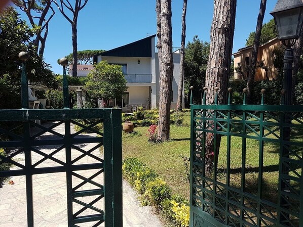 A gated courtyard with a building in the background, surrounded by trees and a well-maintained lawn.