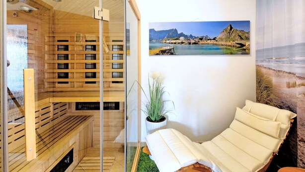 A sauna room with wooden benches and a glass door, a massage chair, and a wall-mounted TV. - Lovely apartment for 4 people with WIFI, TV, terrace and pets allowed (Brakel)