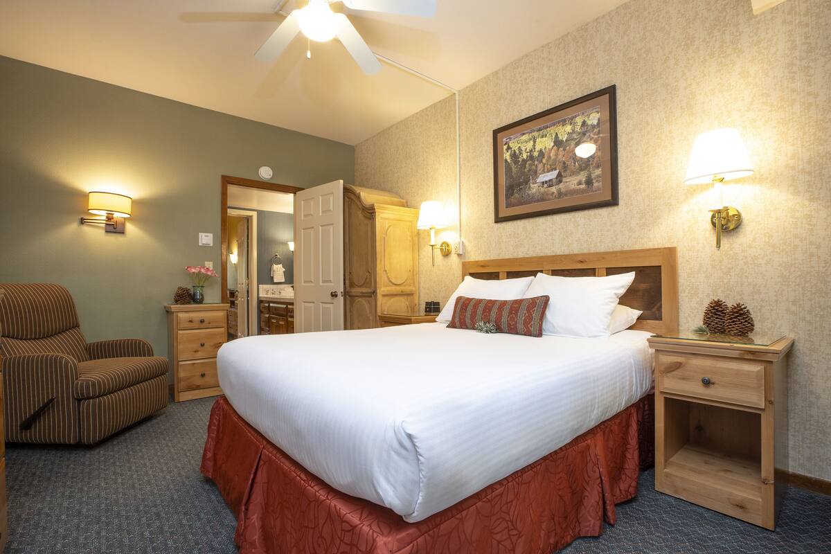 A hotel room with a large bed, a wooden nightstand, a chair, a dresser, and a ceiling fan.