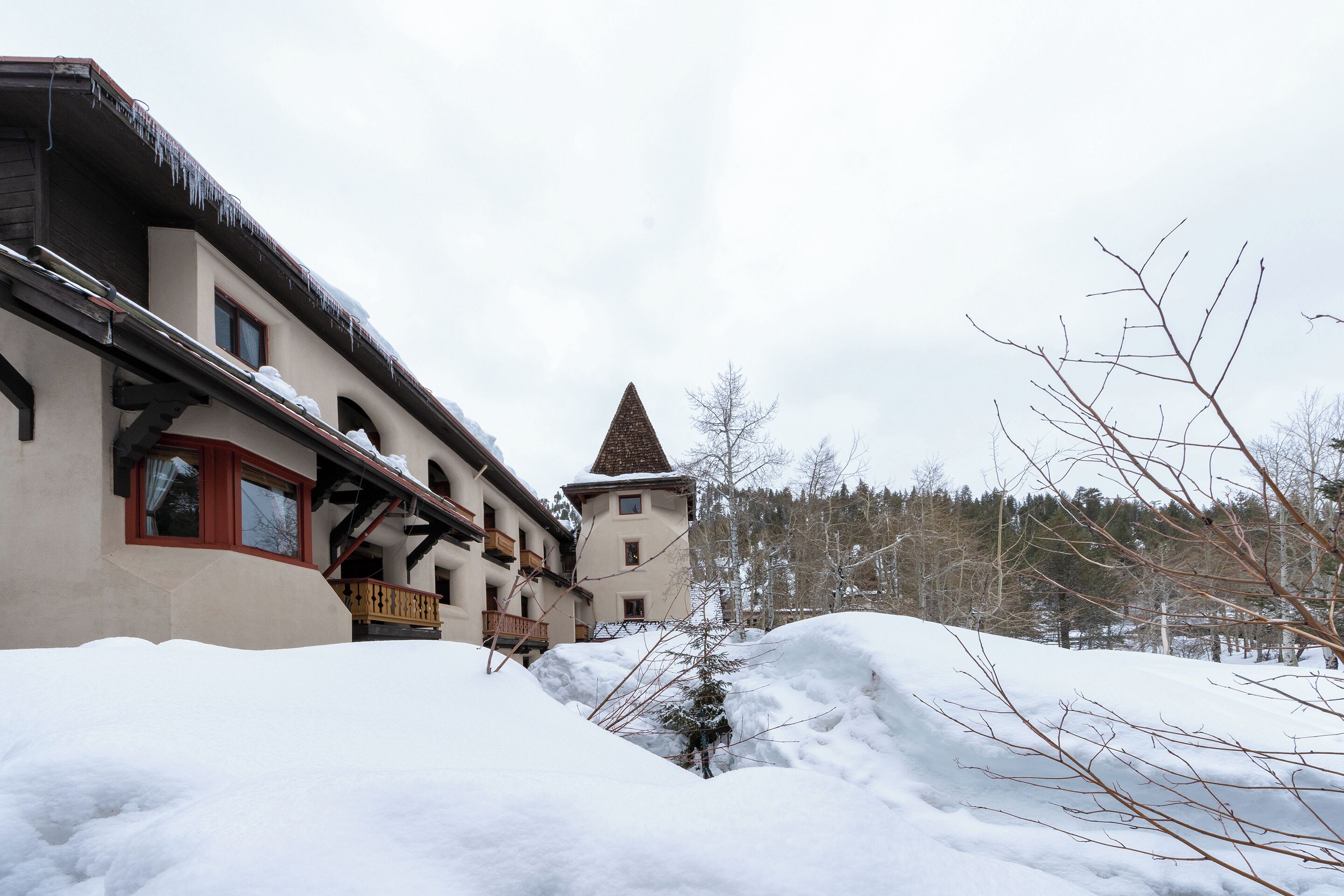 A building with a sloped roof and a small tower, surrounded by snow and trees.