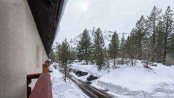 A snow-covered road with parked cars and a view of a forested mountain area.