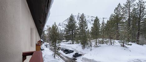 A snow-covered road with parked cars and a view of a forested mountain area.