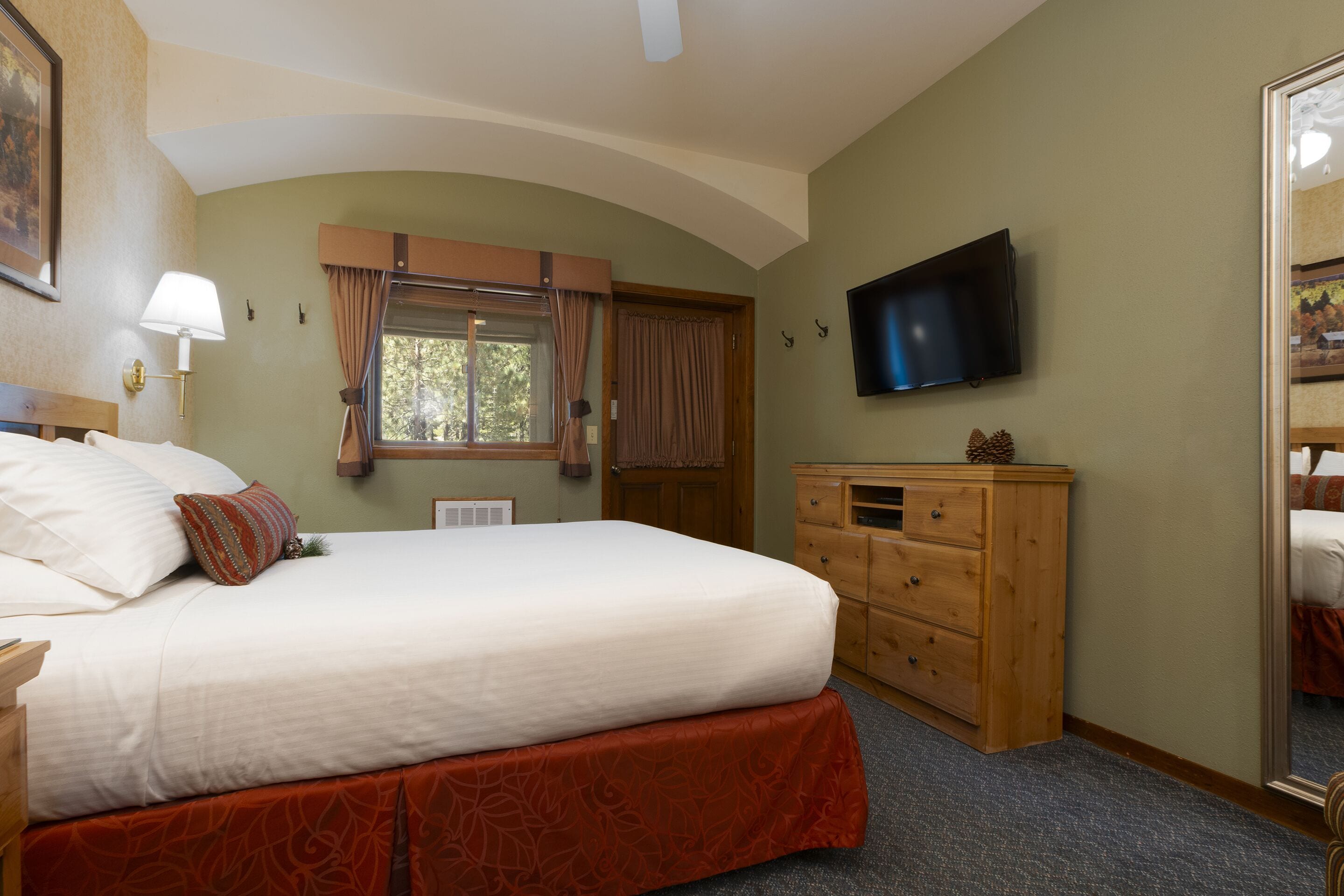 A hotel room with a large bed, a wooden dresser, a flat-screen TV, and a window with curtains.