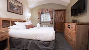 Habitación de hotel con una cama grande, cabecero de madera, cómoda, televisor montado en la pared y una ventana con cortinas.