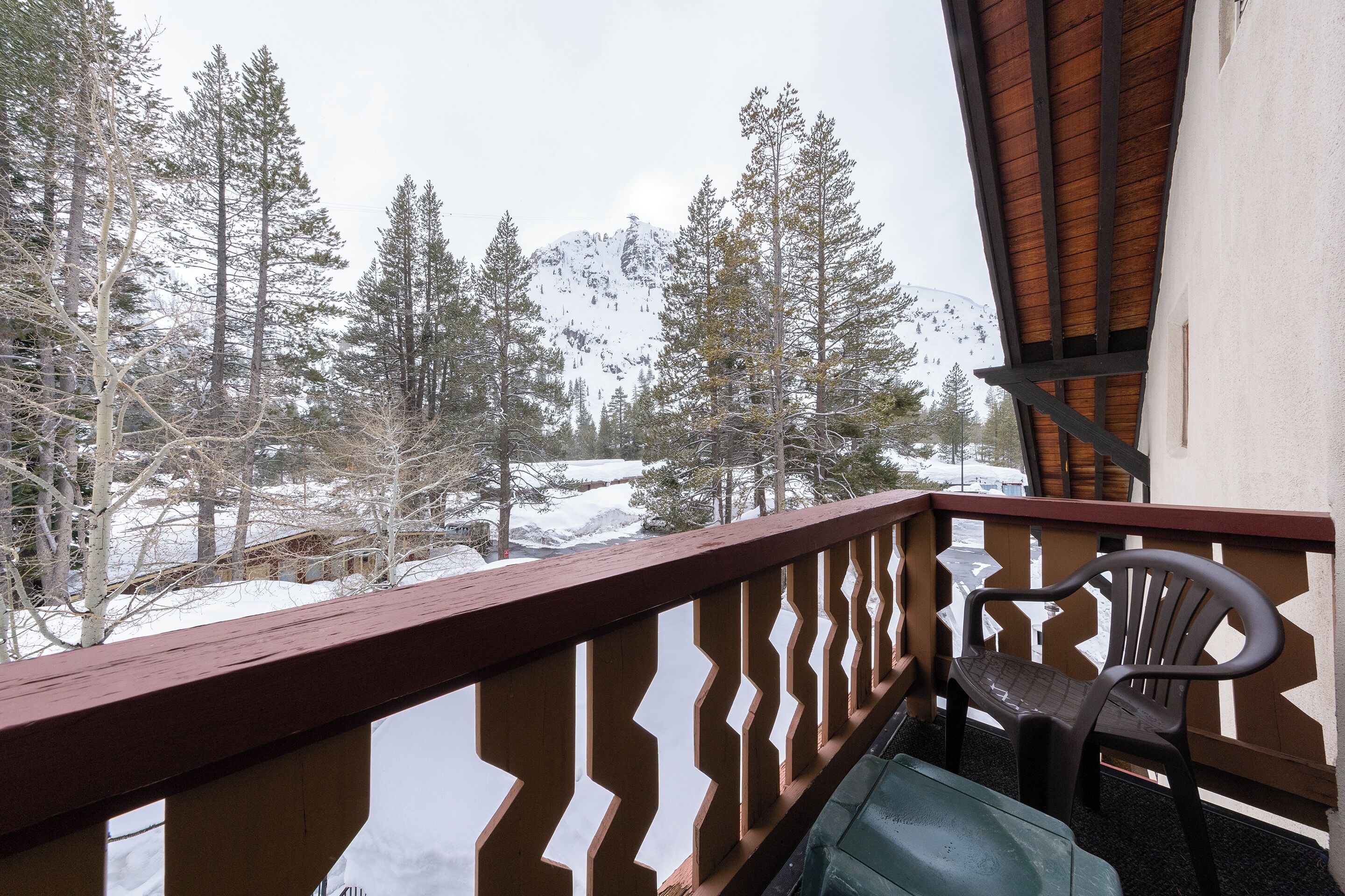 A balcony with a wooden railing, a plastic chair, and a table.