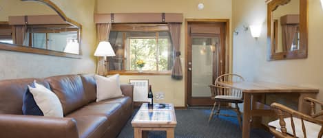 A furnished room with a brown leather sofa, a wooden coffee table, a dining table with chairs, and a large mirror.