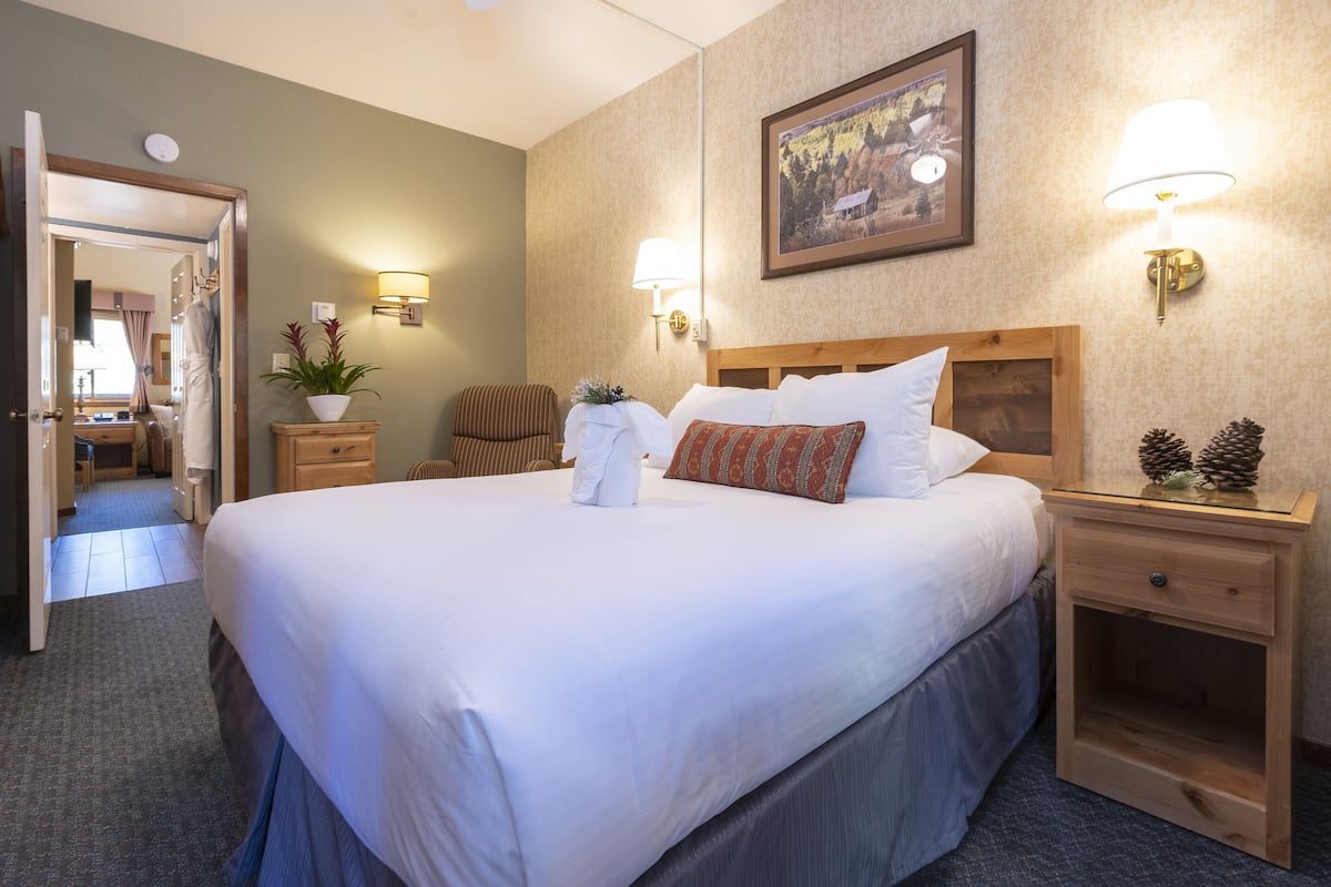 A neatly made bed with white linens, a wooden headboard, and a nightstand with a lamp.
