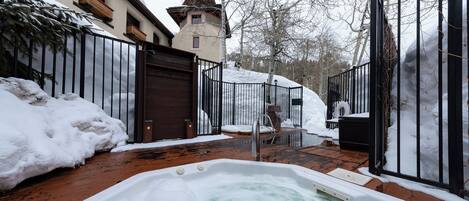 Ett snötäckt utomhusområde med en bubbelpool, ett trädäck och en byggnad med ett torn.