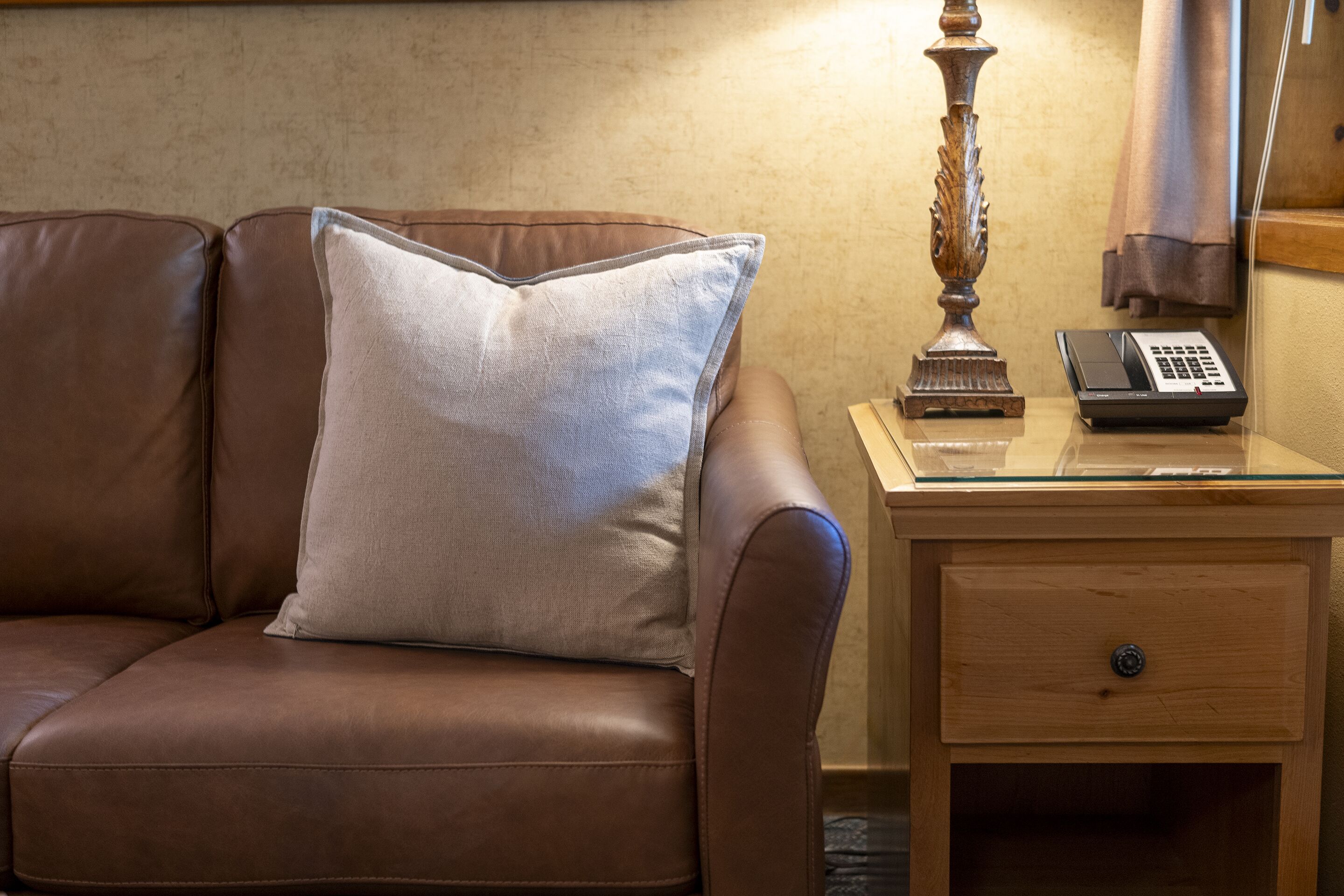 Un canapé en cuir marron avec un seul coussin, une table de chevet en bois avec un téléphone et une lampe décorative.