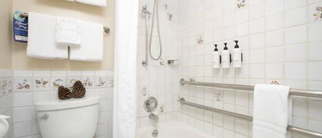 Une salle de bain équipée de toilettes, d’une baignoire et d’une douche. Des serviettes et des articles de toilette sont accrochés au mur.