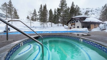 A swimming pool with a 3 ft depth marker, surrounded by snow-covered trees and a building with a sloped roof.