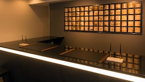 Ein moderner Empfangstresen mit Glastischplatte, ein gerahmtes Kunstwerk darüber und ein kleiner Tisch mit einem weißen Gegenstand.