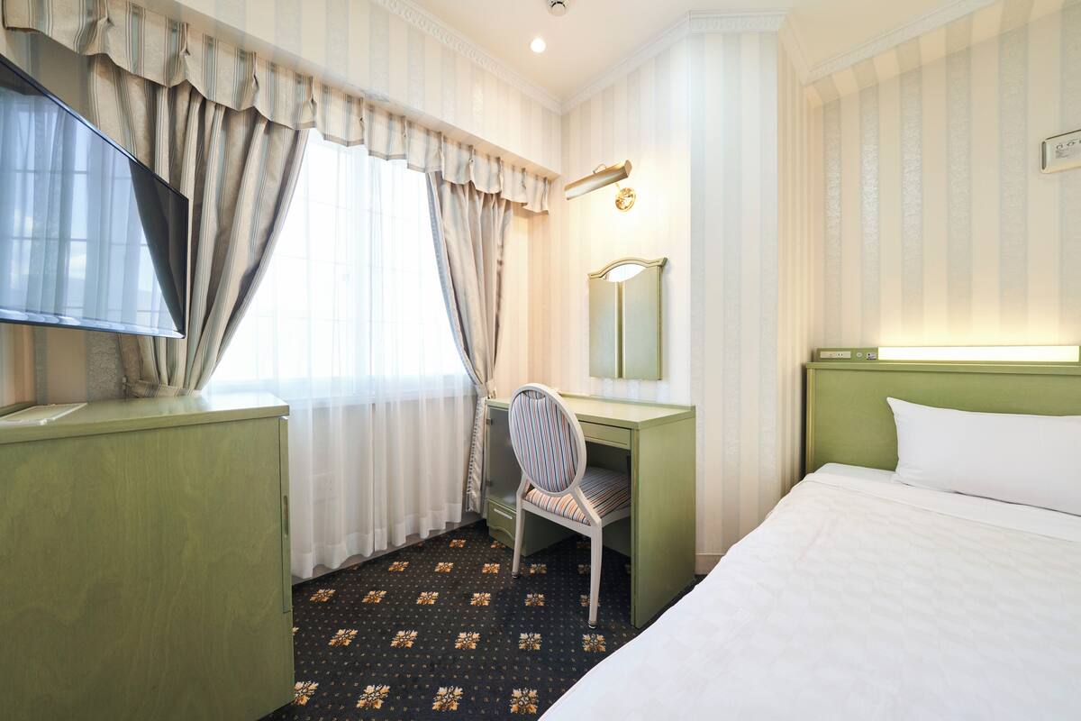 A hotel room with a bed, a desk, a chair, a television, a mirror, and a window with curtains.