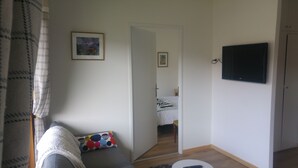 A small, sparsely furnished room with a bed, a TV, and a door leading to another room. - Two rooms in Thonon les Bains (Thonon-les-Bains)